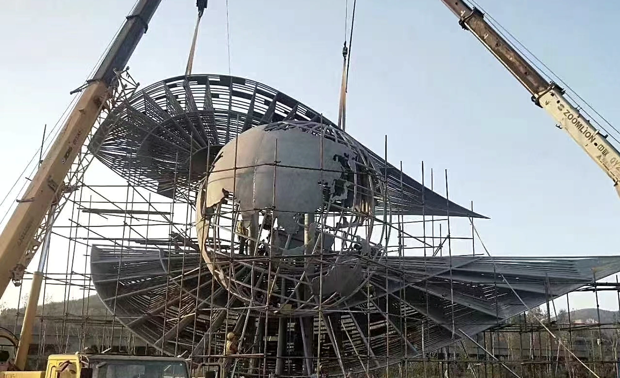 Large metal landmark sculpture core and segmented wings under construction with temporary access and cranes