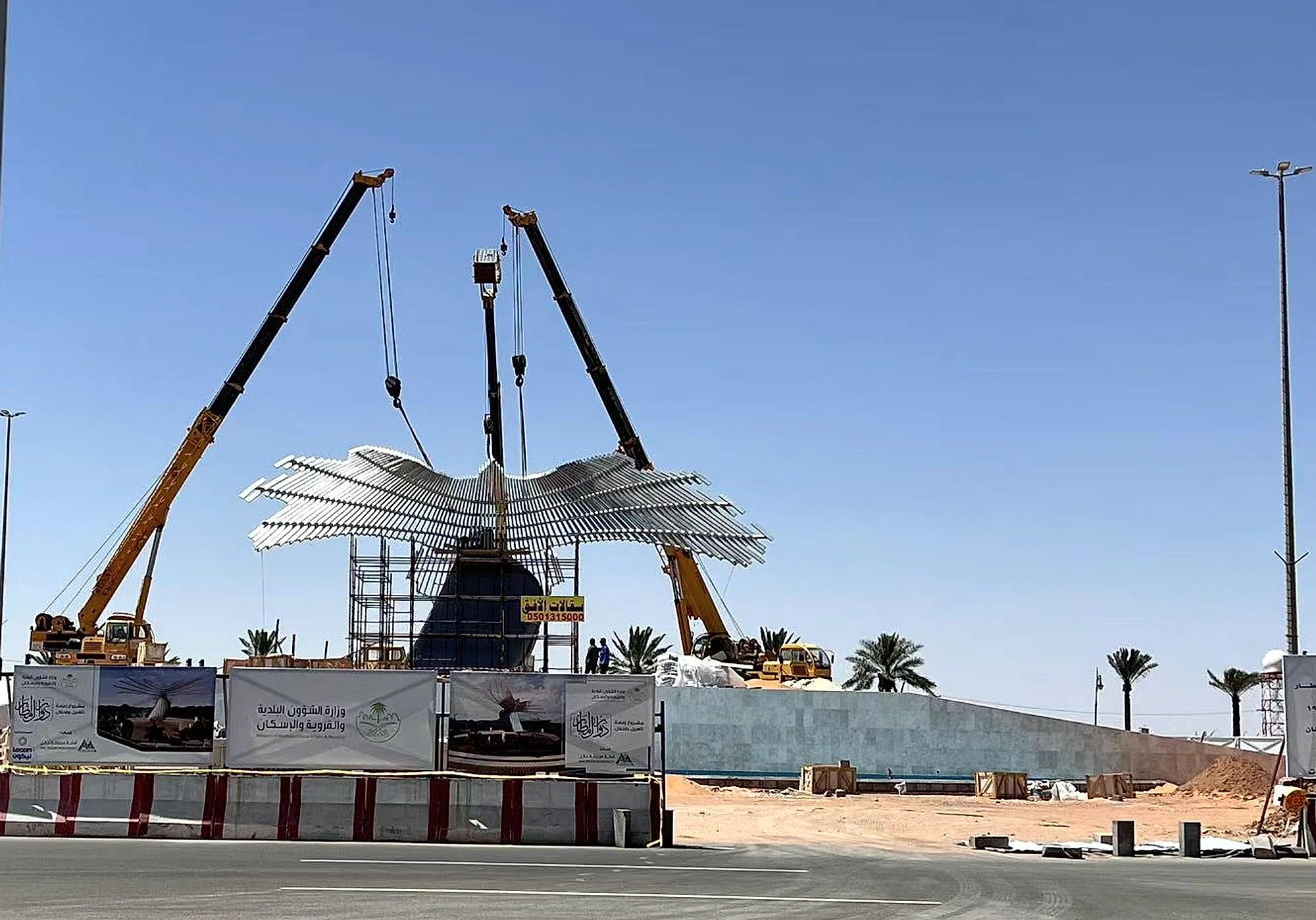 Large stainless steel flying-bird landmark sculpture being lifted into position by cranes at a Middle East public plaza