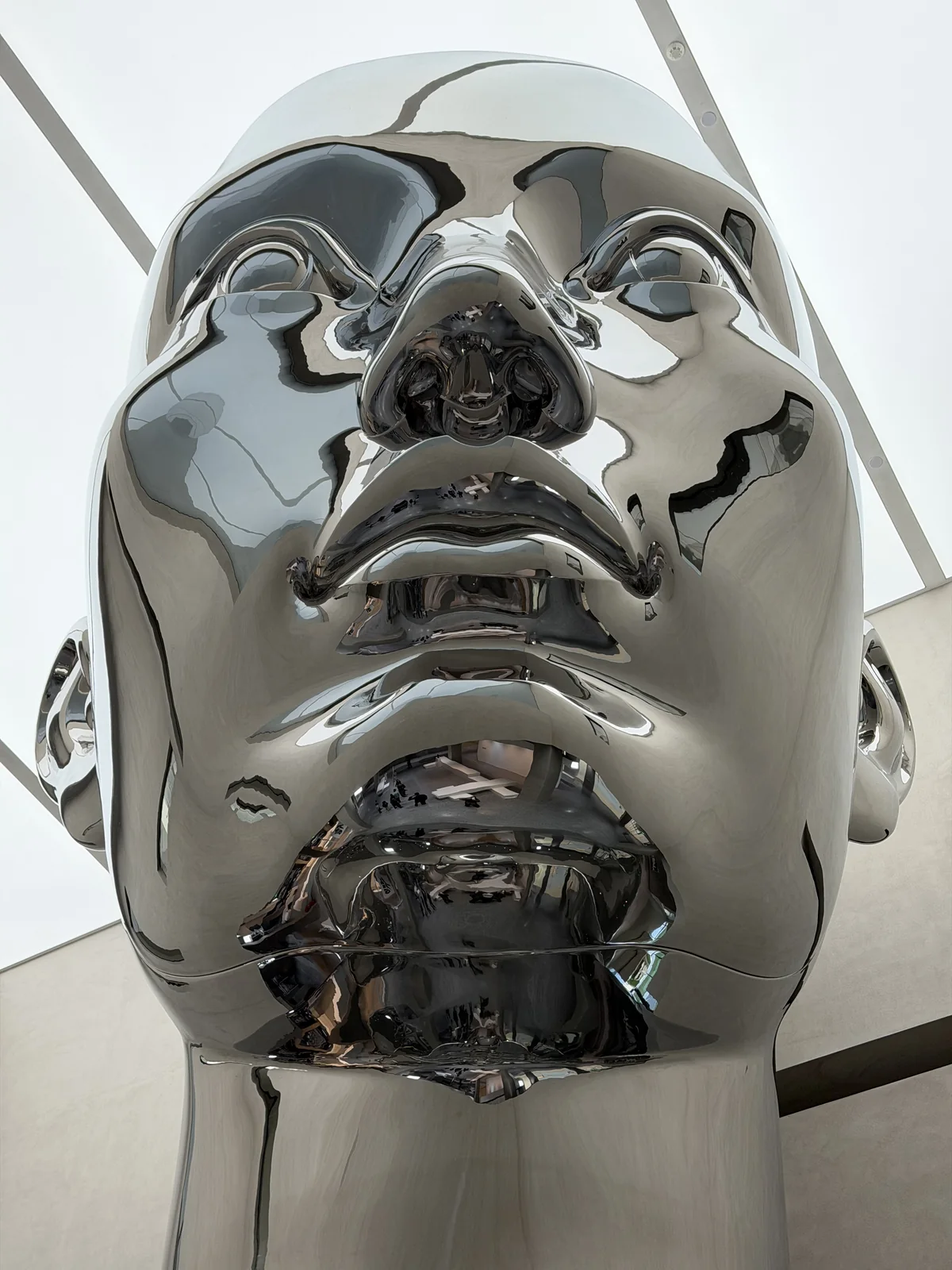 Front view of mirror polished stainless steel sculpture reflecting ceiling lights and interior architecture