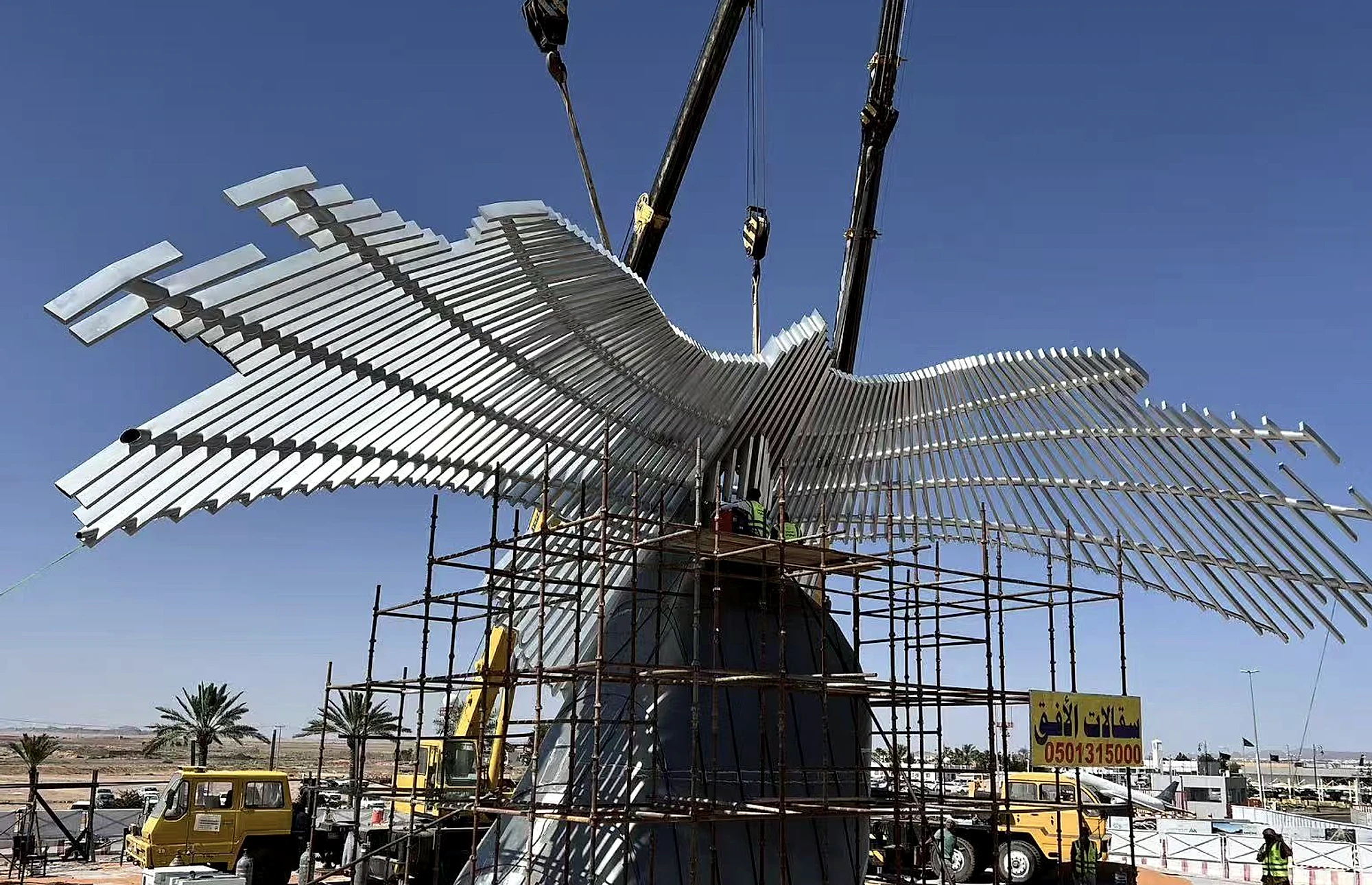 Parallel stainless steel wing slats being aligned during construction of a large flying-bird landmark sculpture